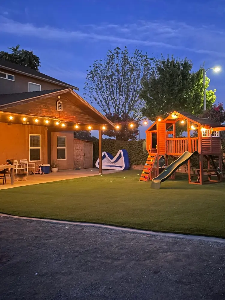 Back yard at dusk with a covered patio, string lights and artificial grass built by Millenium in Perris, CA