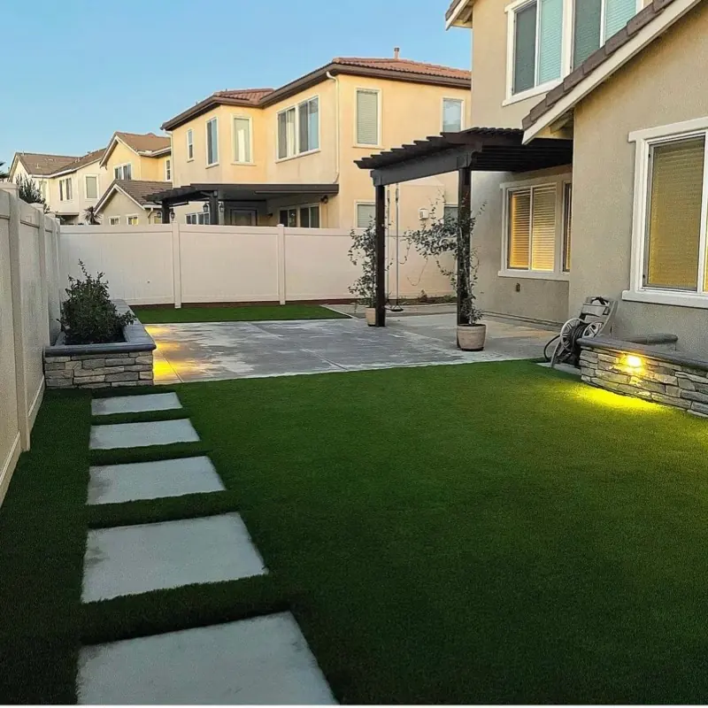 Concrete stepping pads, a lit planter wall and artificial grass beside a two-story home